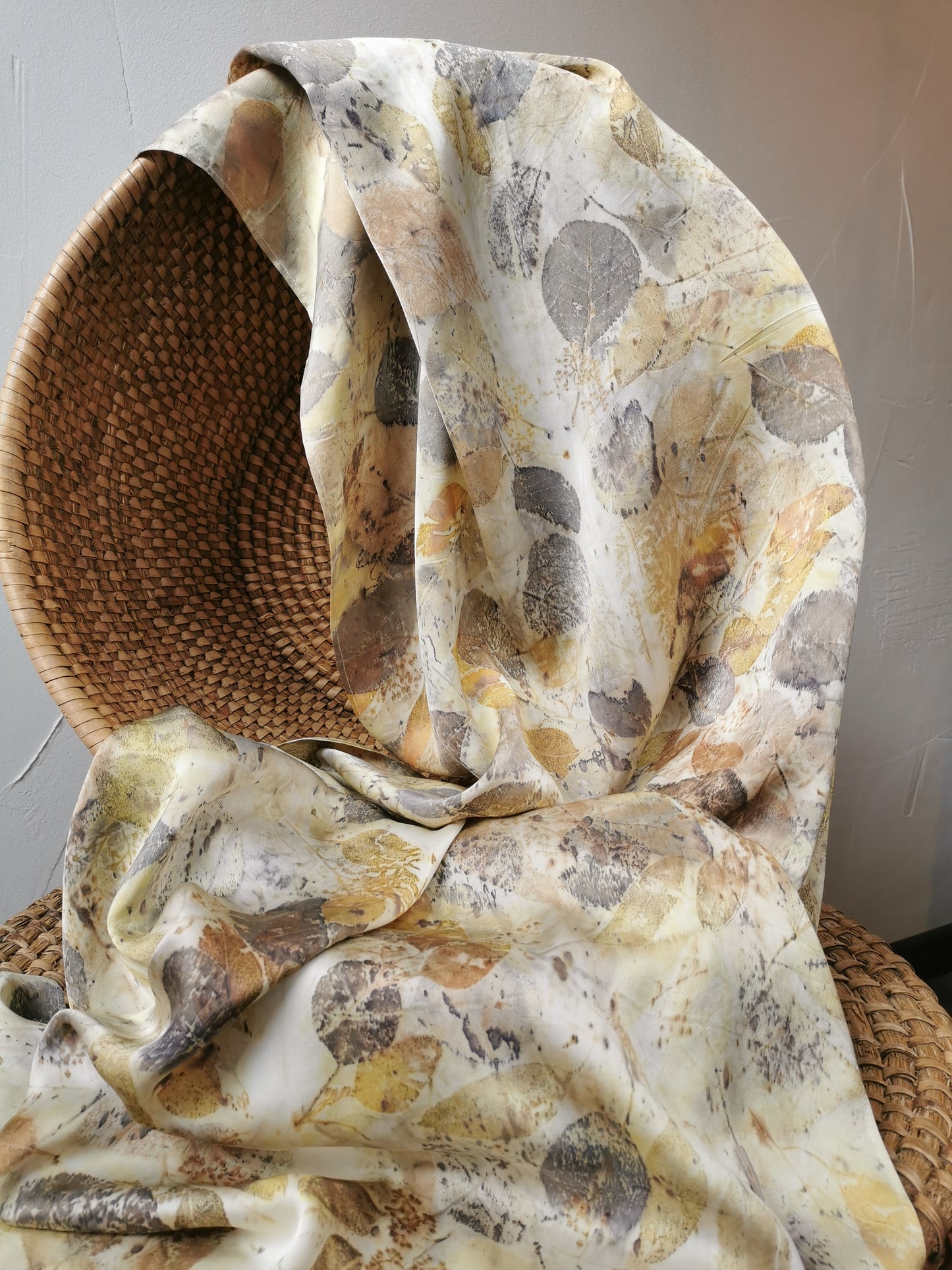 leaf eco-printed silk scarf with leaf pattern draped over a woven chair against a neutral background
