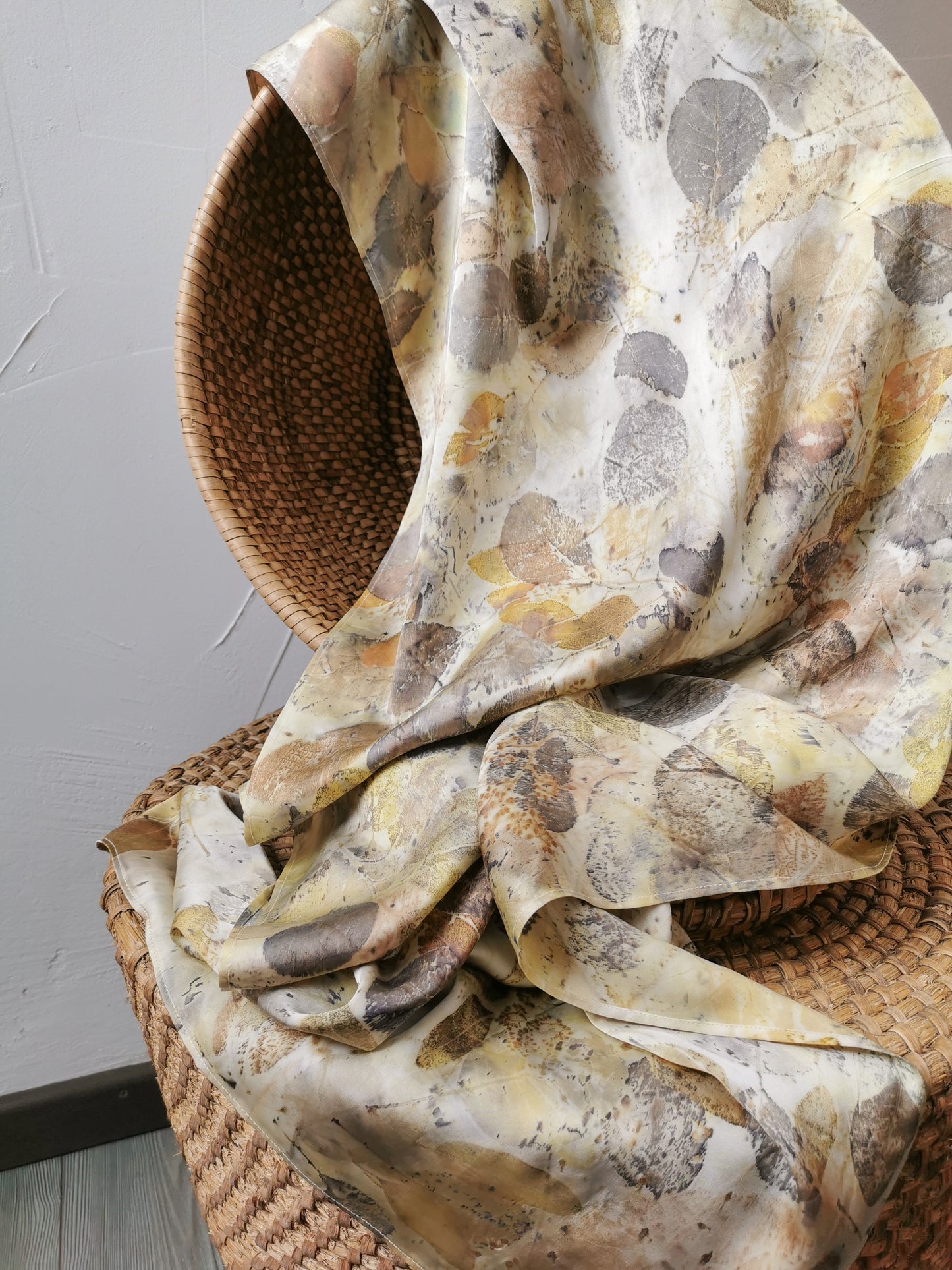 leaf eco-printed silk scarf with leaf pattern draped over a woven basket on a neutral background