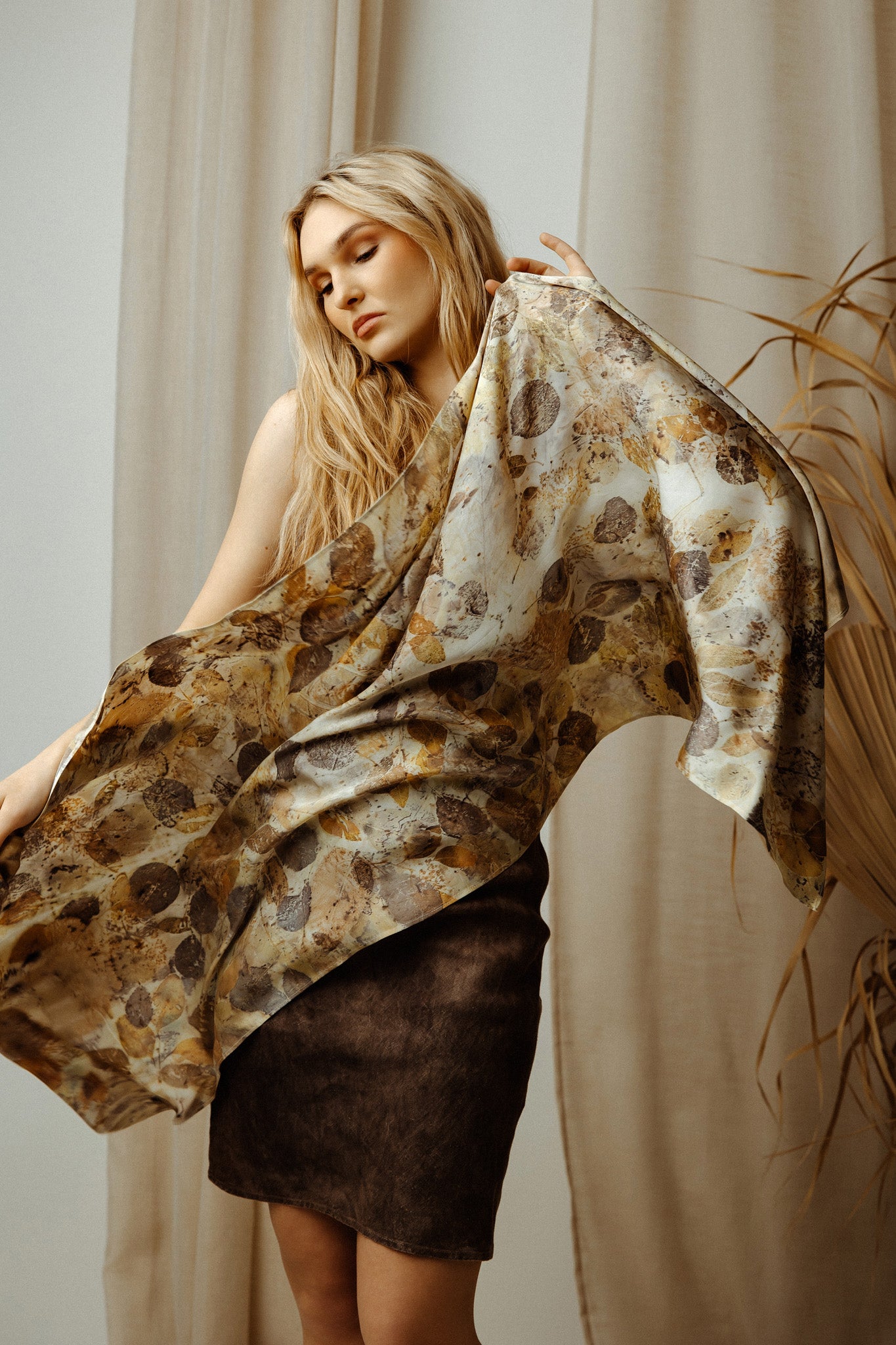 Woman holding a patterned scarf in front of a neutral background