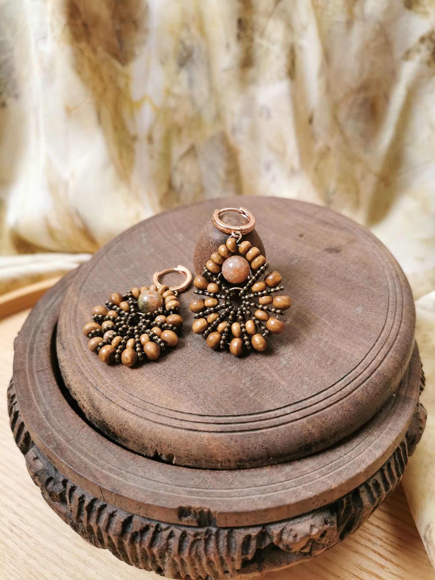 Pair of gold and brown beaded earrings on a wooden surface