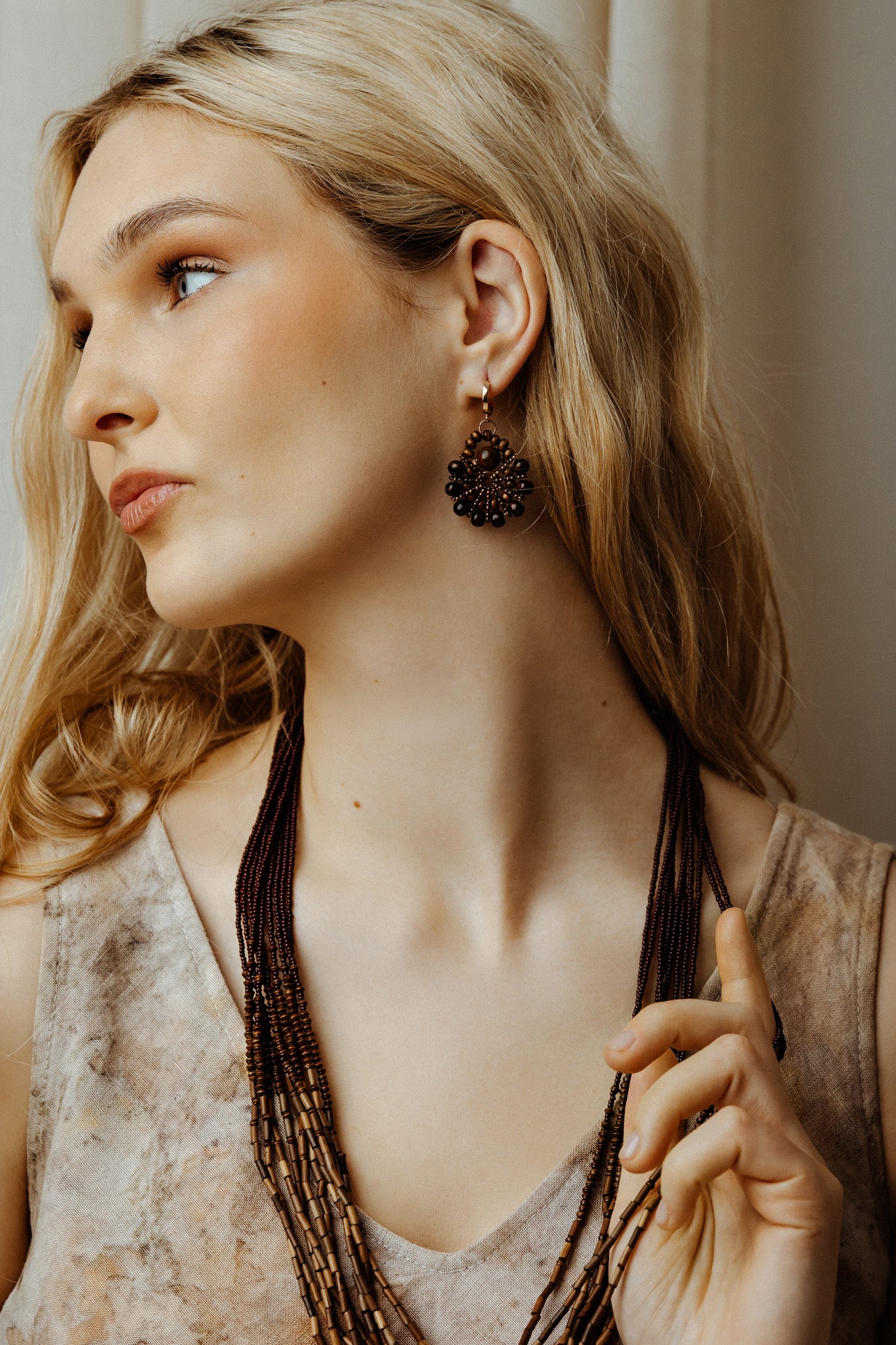 Woman wearing a long boho bead multilayer necklace and earrings, looking to the side.