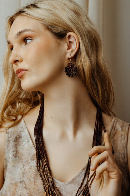 Woman wearing a long boho bead multilayer necklace and earrings, looking to the side.