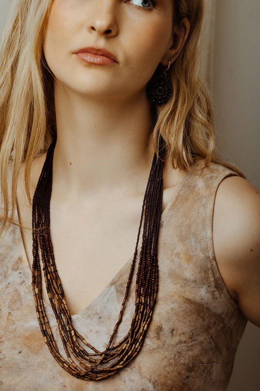 Woman wearing a long boho bead multilayer necklace against a neutral background