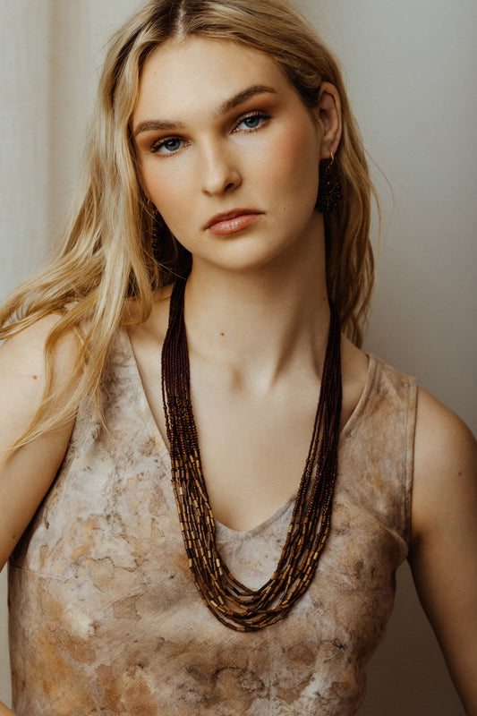 Woman wearing a patterned top and multiple necklaces against a neutral background
