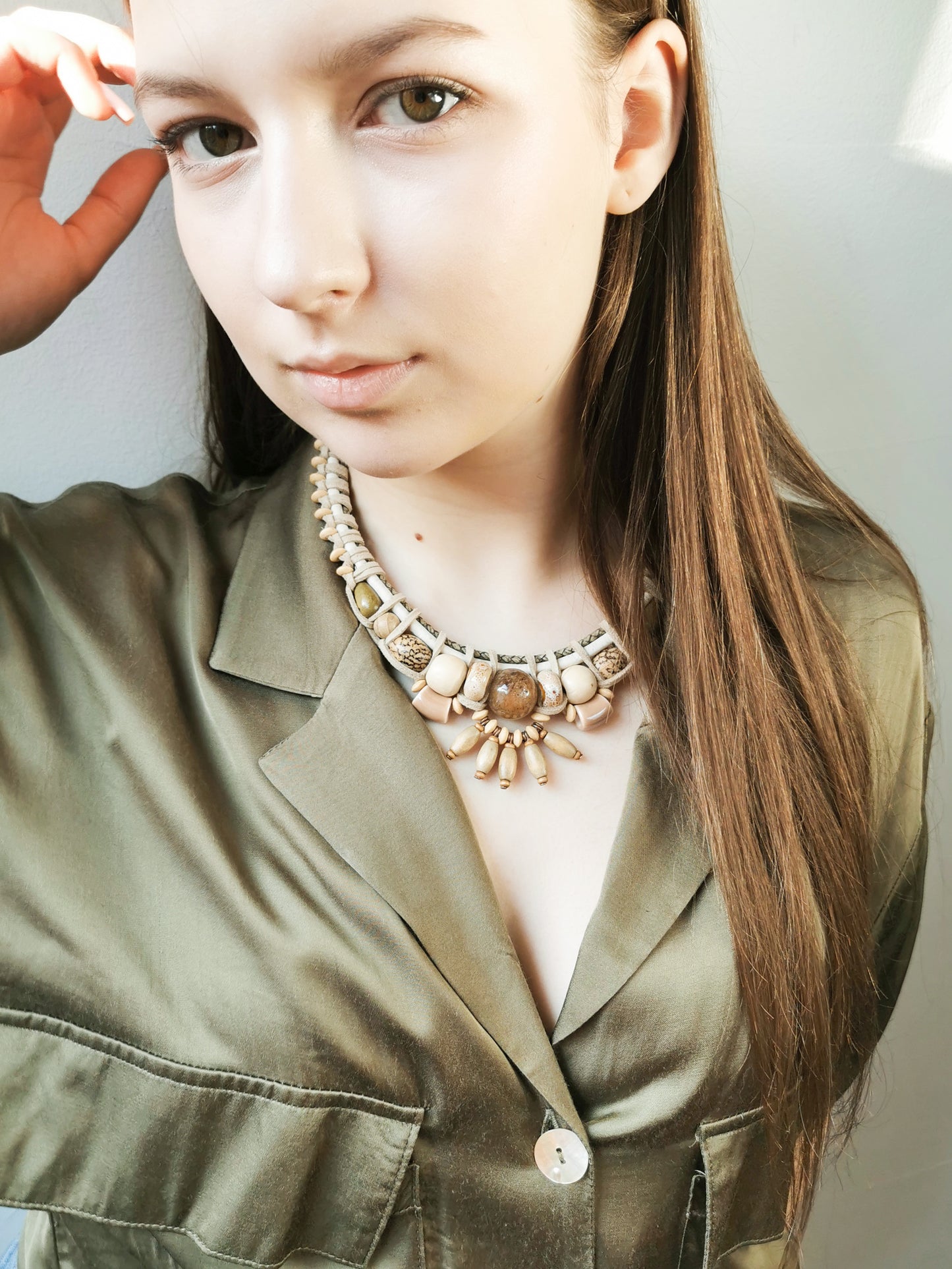 Woman wearing a green jacket and a decorative necklace against a neutral background