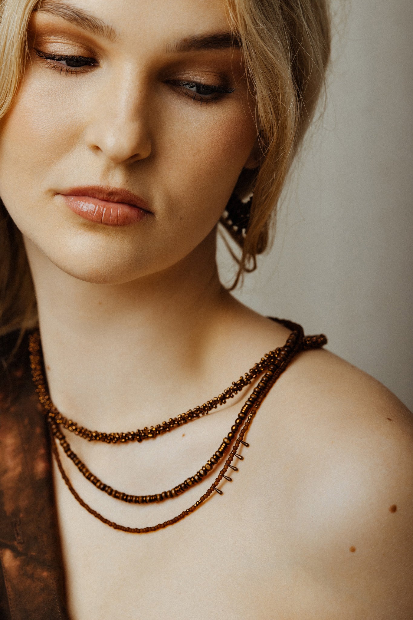 Close-up of a woman wearing a beaded necklace against a neutral background