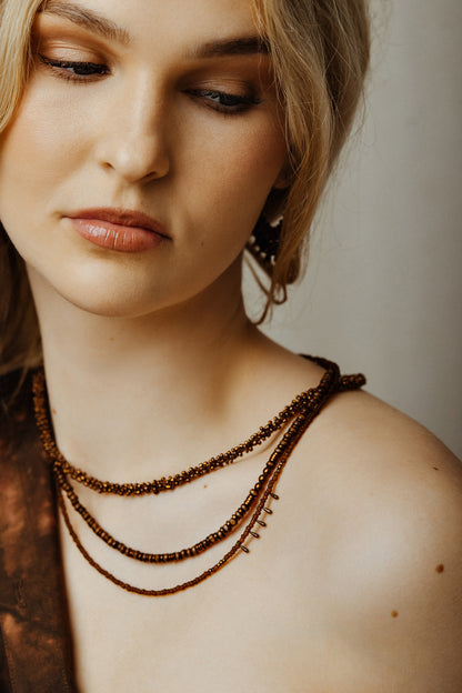 Close-up of a woman wearing a beaded necklace against a neutral background