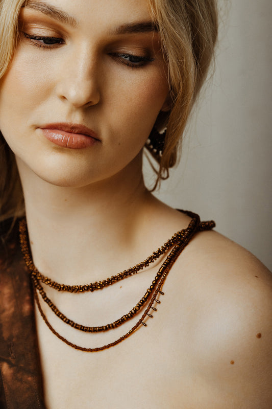 Close-up of a woman wearing a beaded necklace against a neutral background