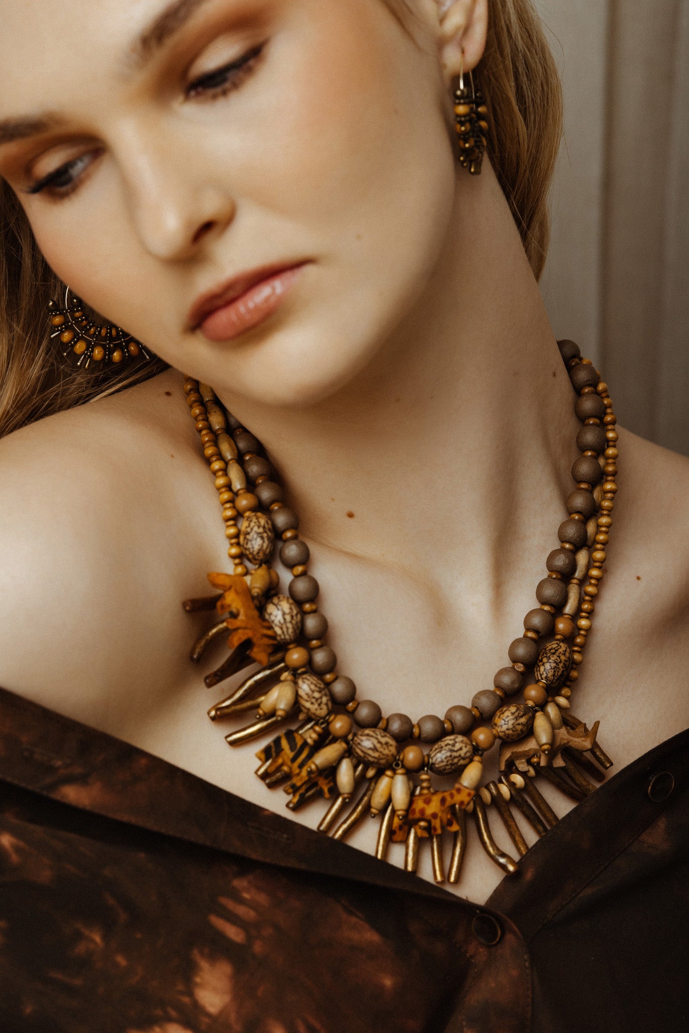 Close-up of a model wearing wild animal charm necklace and earrings with a neutral background