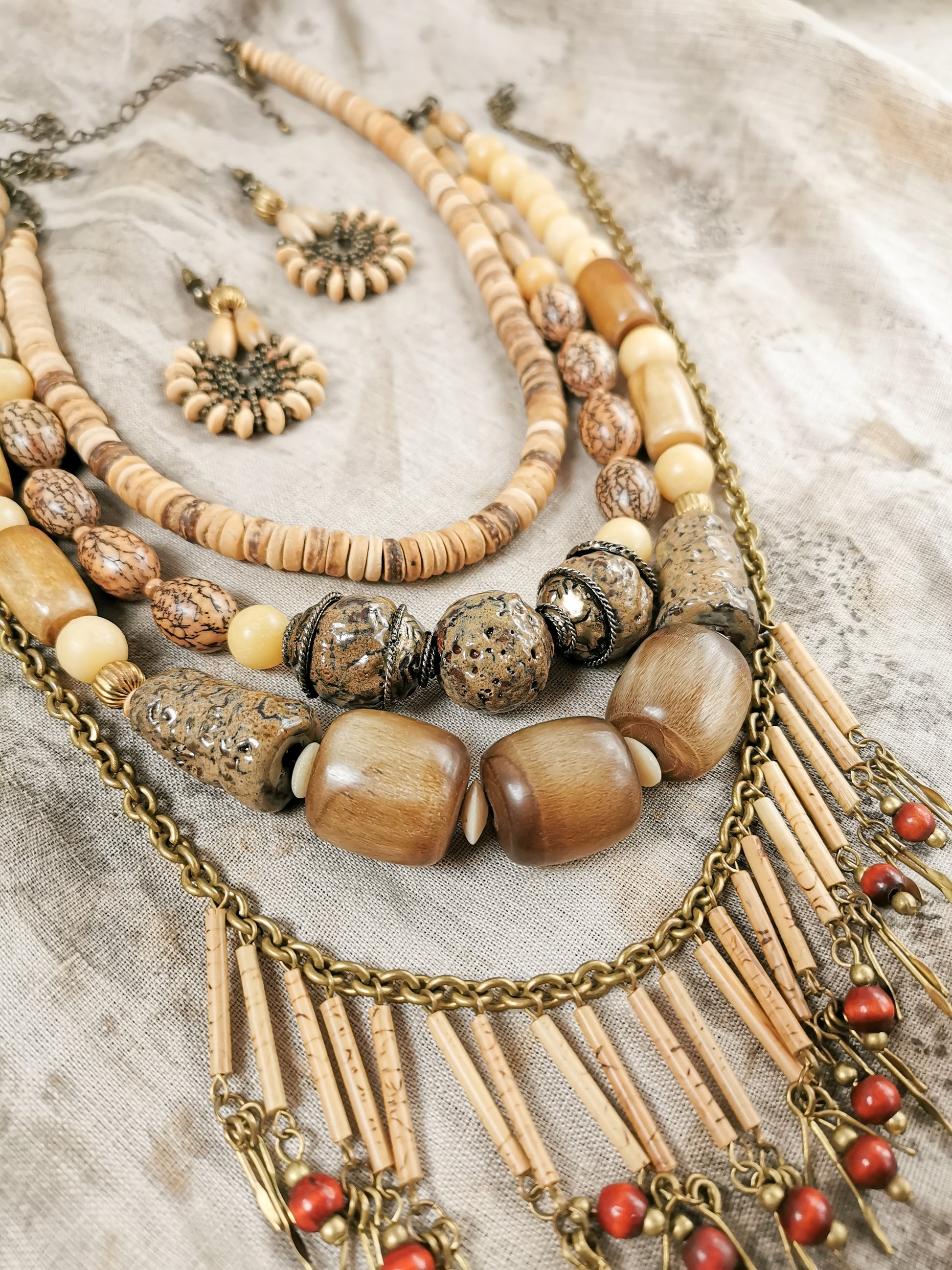 Collection of beaded necklaces and earrings on a textured fabric background