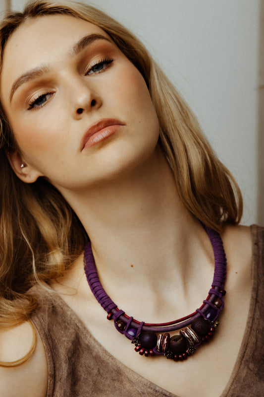 Woman wearing a purple beaded necklace against a neutral background