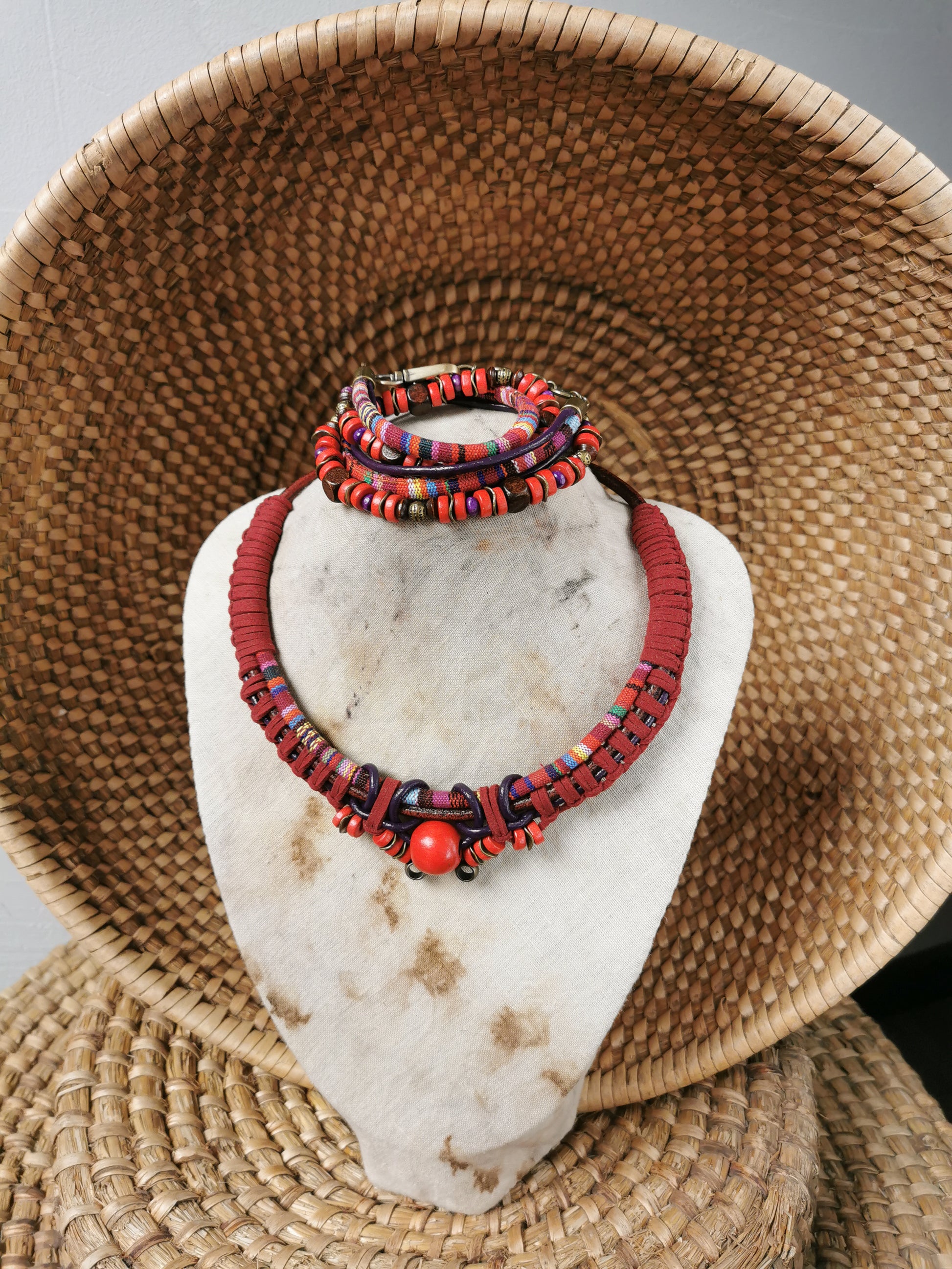 Red beaded necklace and bracelets on a white stone stand with a woven basket background