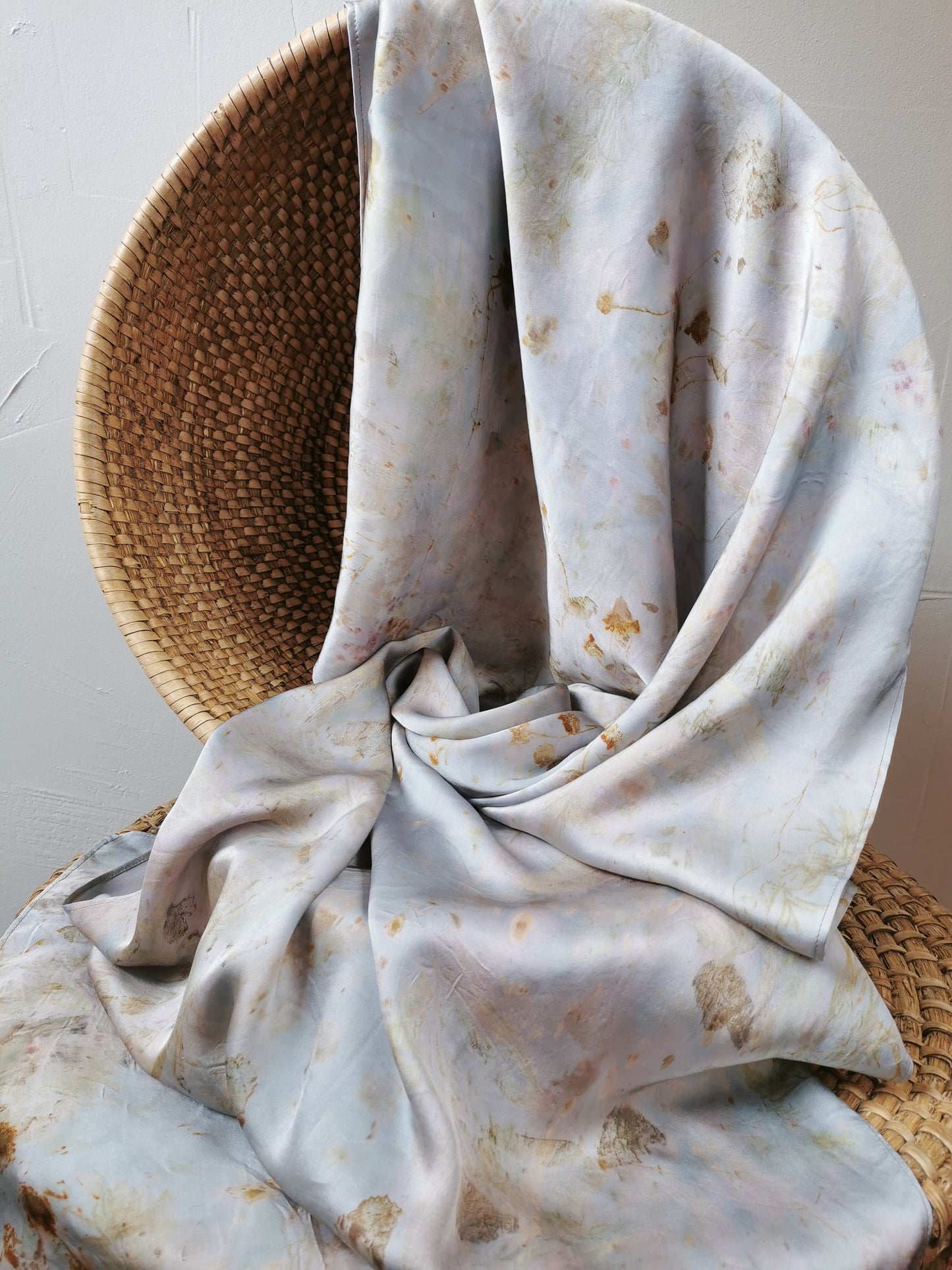 silver botanical dye silk shawl on a woven basket against a light background
