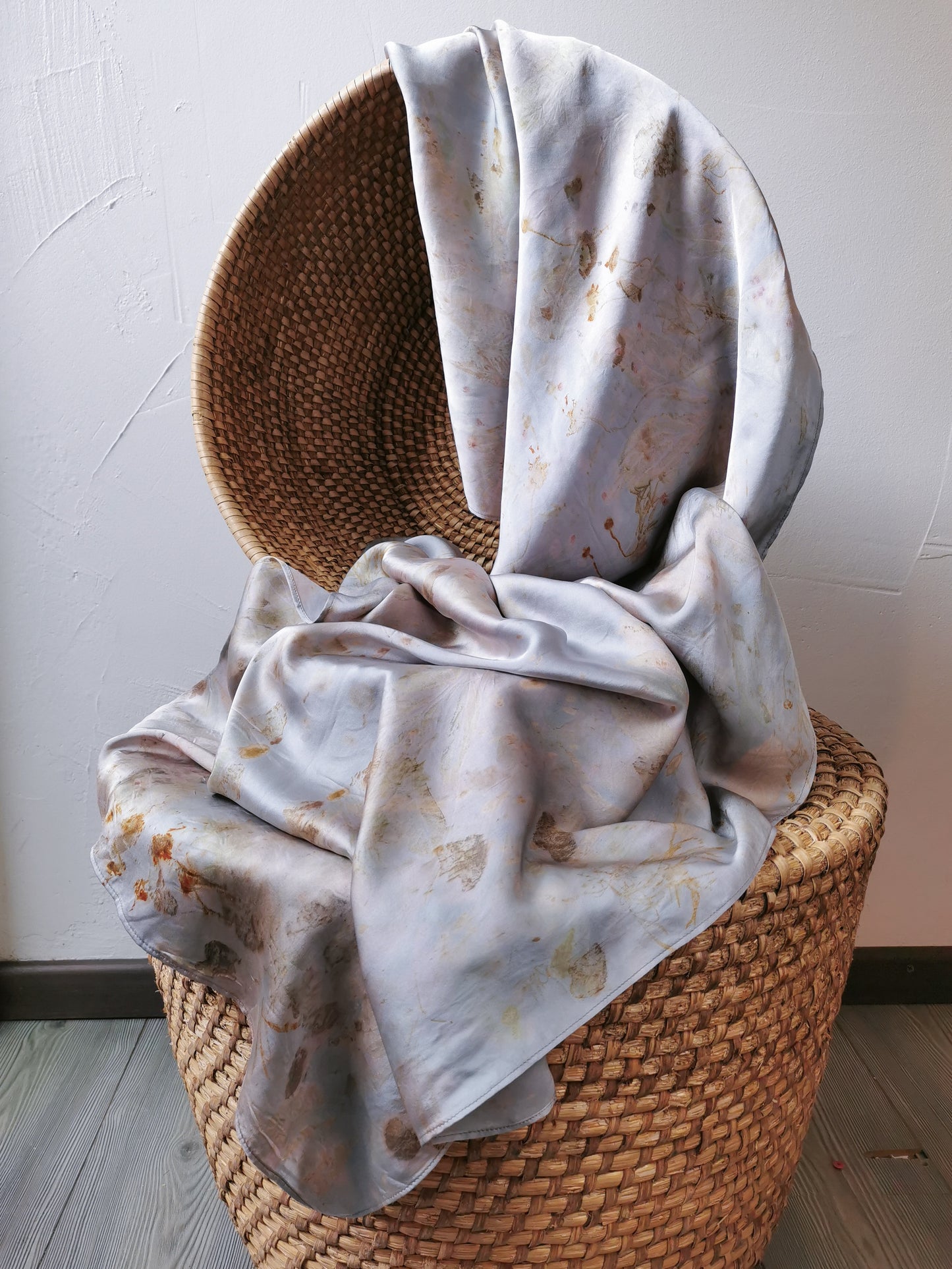 Woven basket with silver botanical dye silk shawl draped over it against a plain wall.
