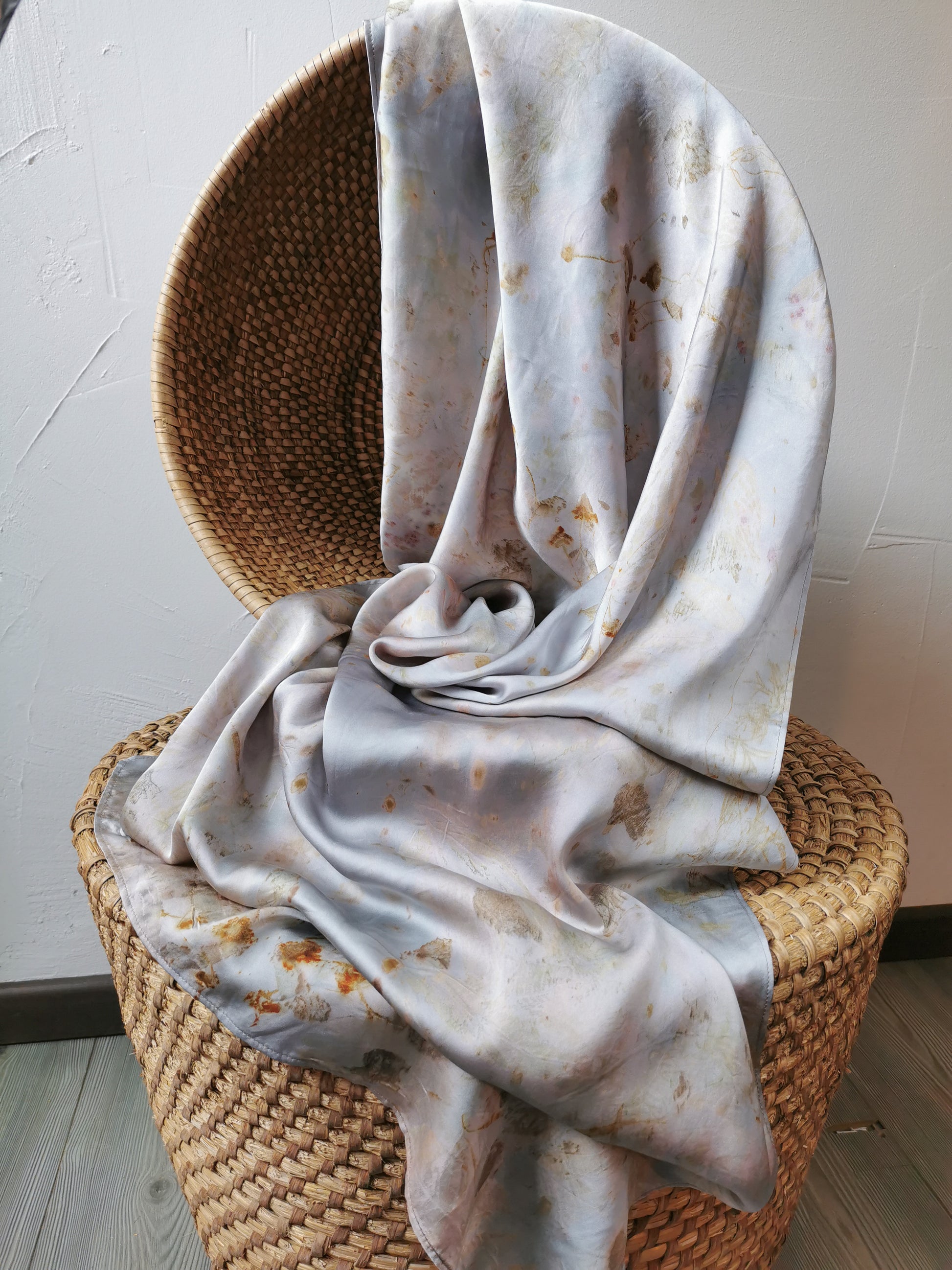 silver botanical dye silk shawl draped over a wicker chair against a plain wall.