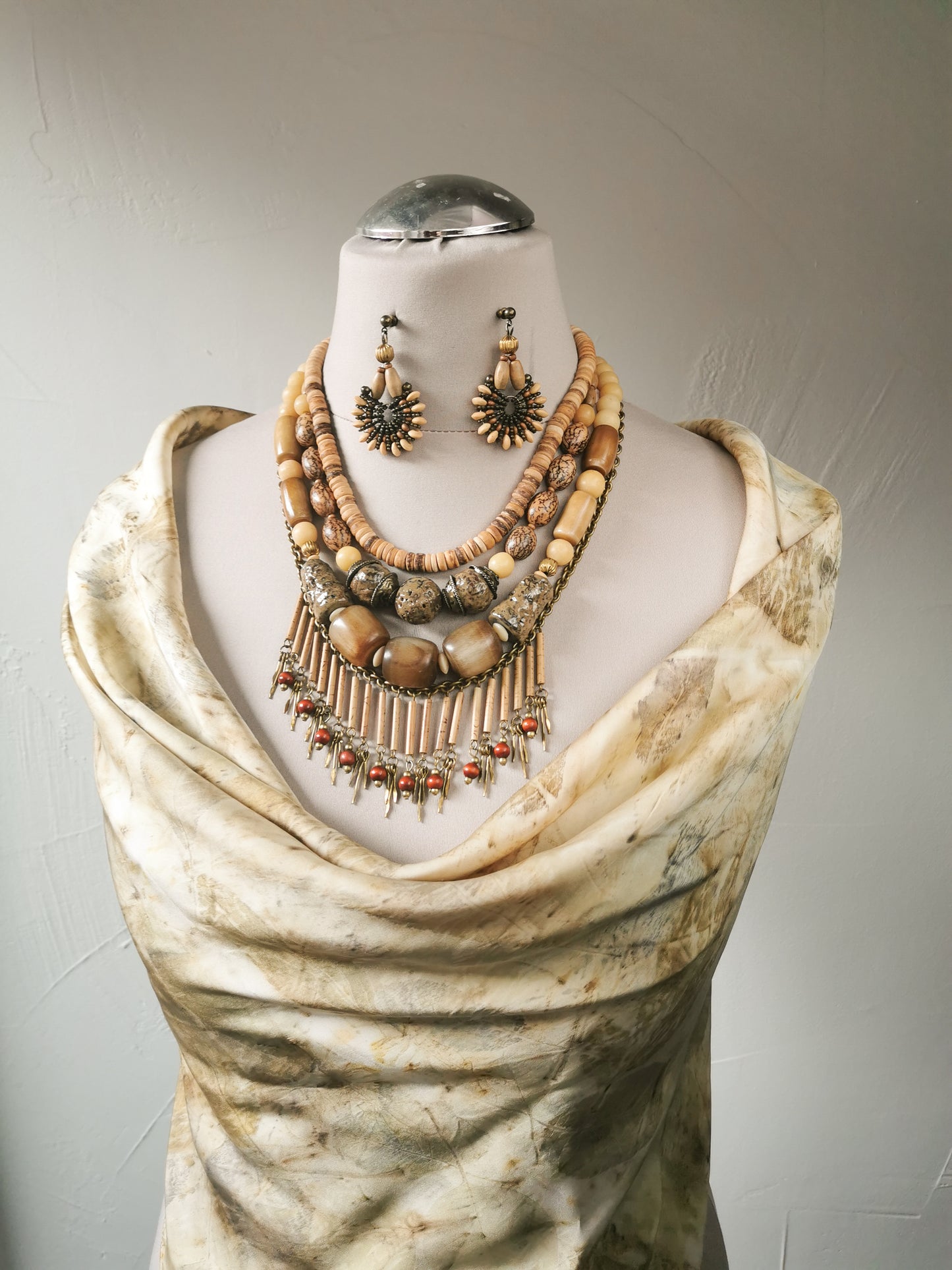 Mannequin wearing a beige draped garment with a necklace and earrings on a plain background