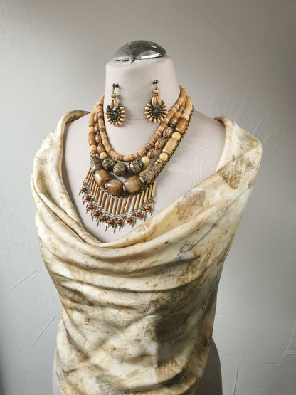 Mannequin wearing a draped fabric with a necklace and earrings on a plain background