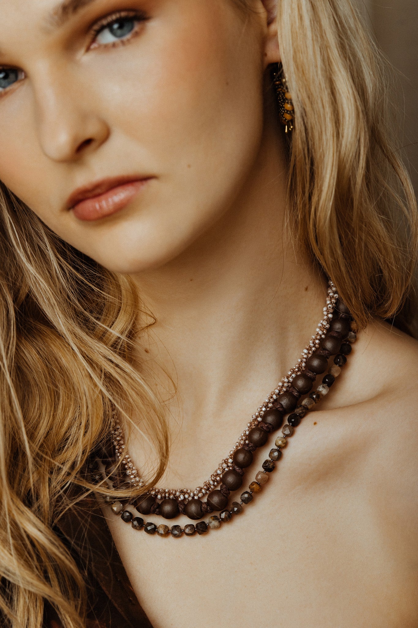 Close-up of a woman wearing a brown beaded necklace with a neutral background