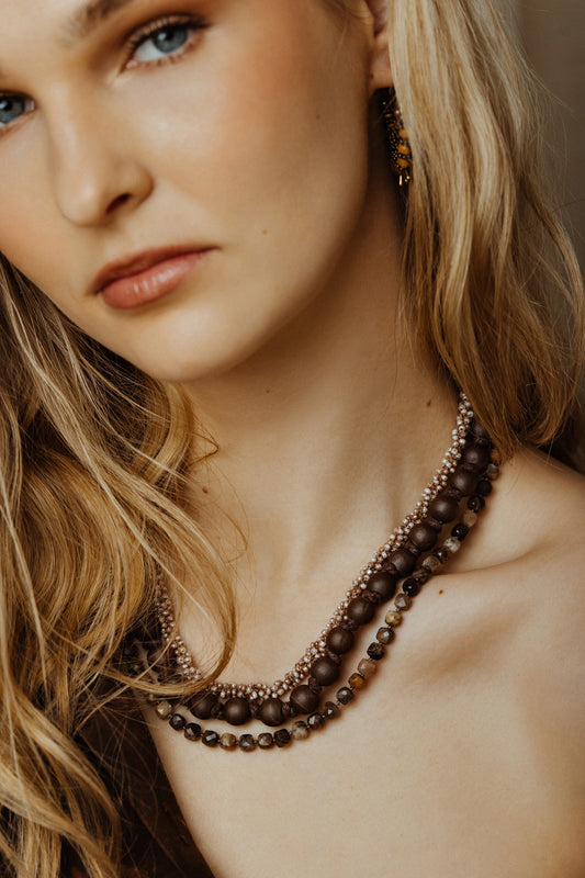 Close-up of a woman wearing a brown beaded necklace with a neutral background