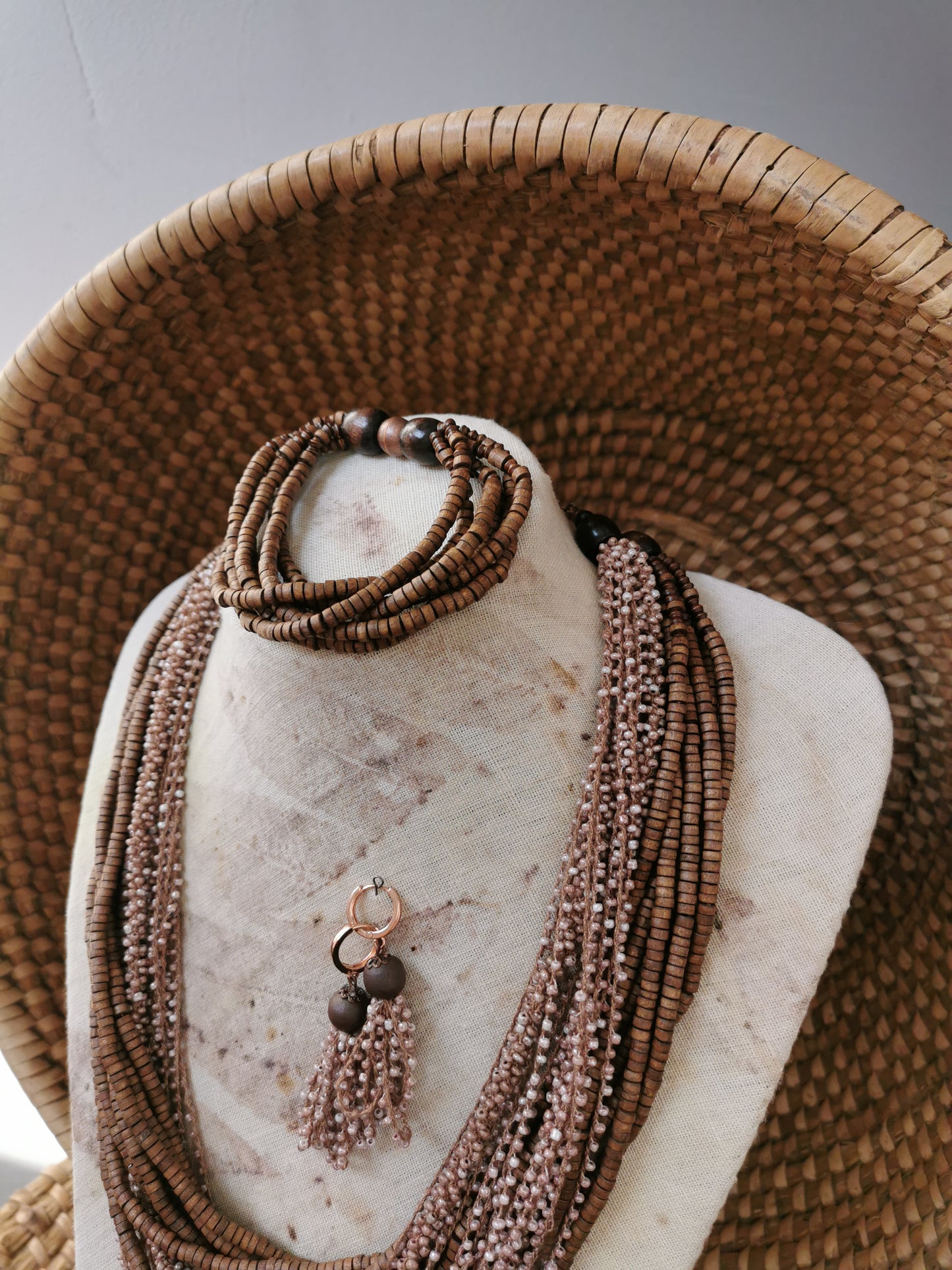 Brown beaded necklace on a mannequin bust with a woven basket in the background