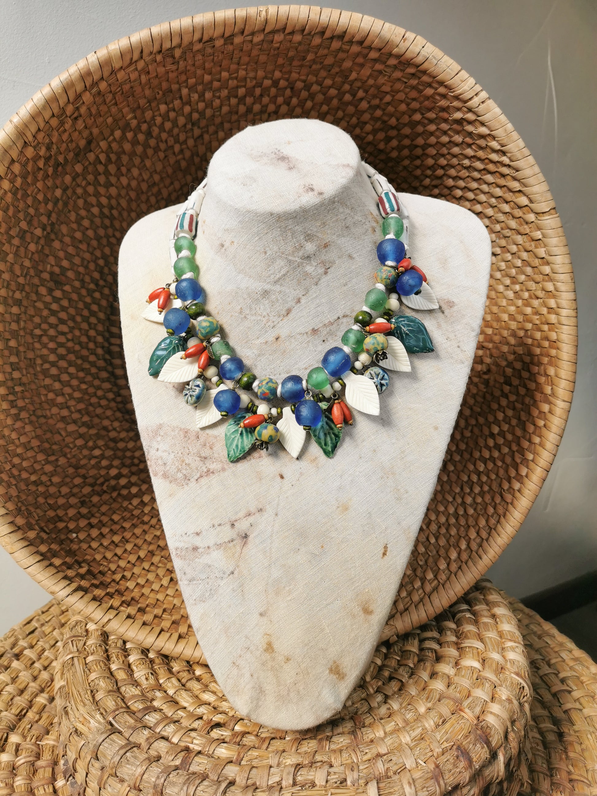 Colorful whimsical floral charm necklace  on a stone bust with a woven basket background