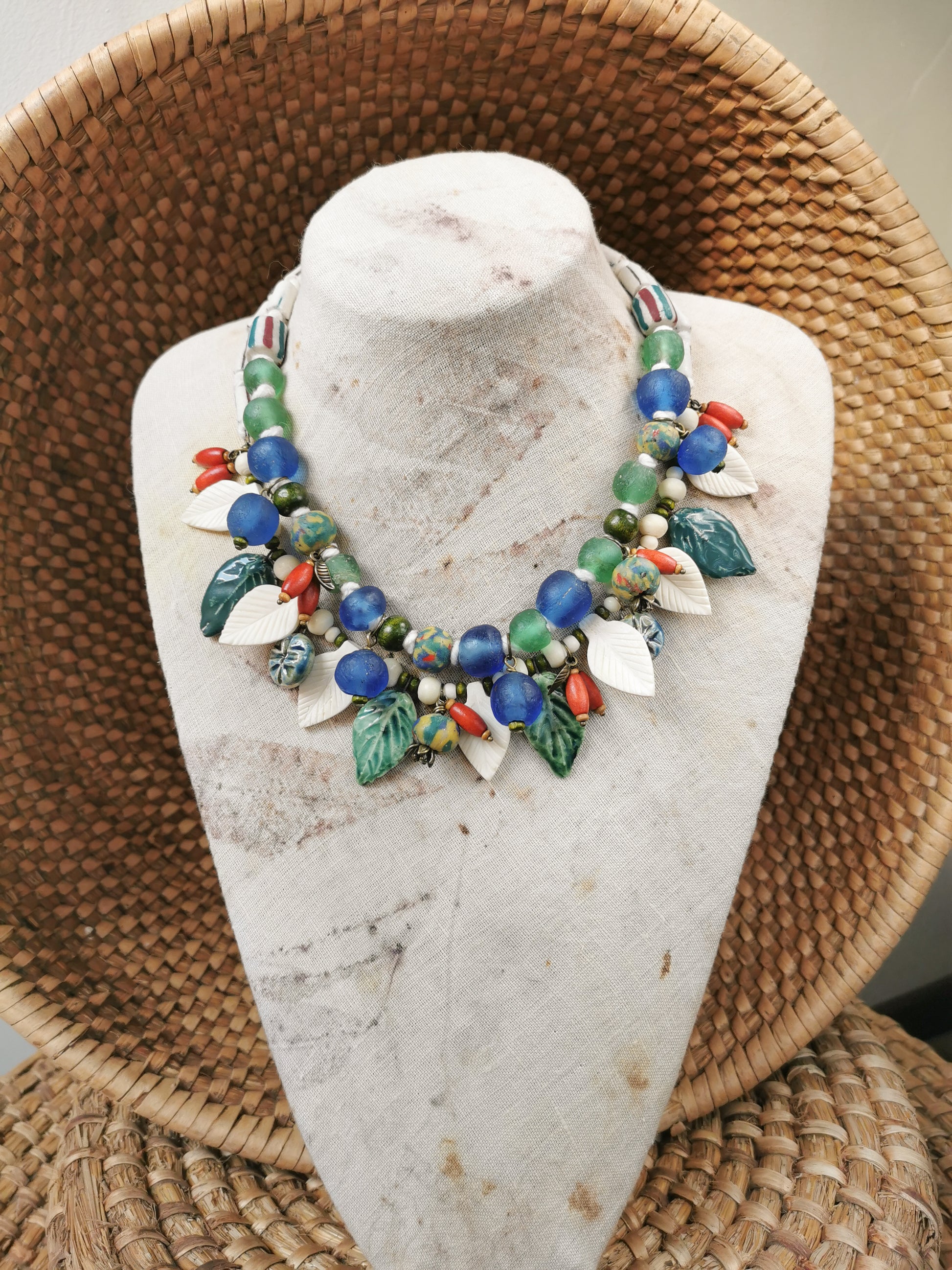 Colorful whimsical floral charm necklace  on a marble bust with a woven basket background