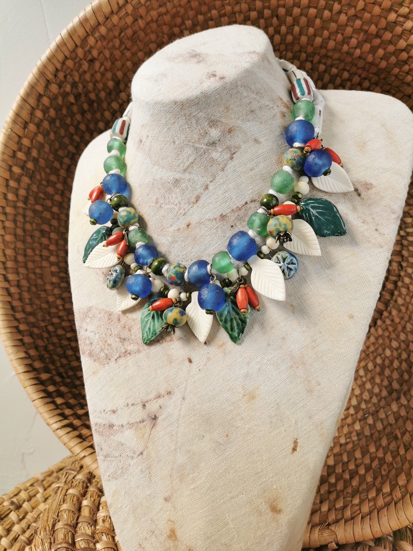 Colorful whimsical floral charm necklace  on a stone stand with a woven background
