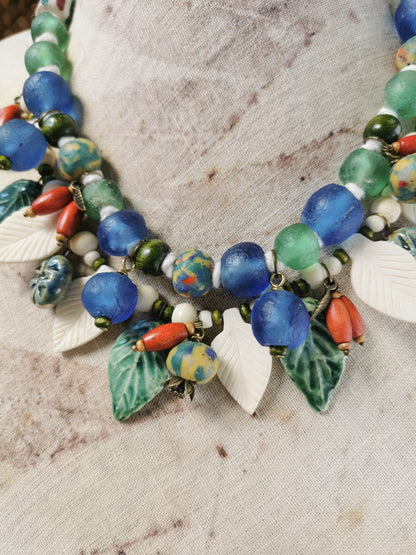Colorful whimsical floral charm necklace with leaf-shaped pendants on a textured fabric background
