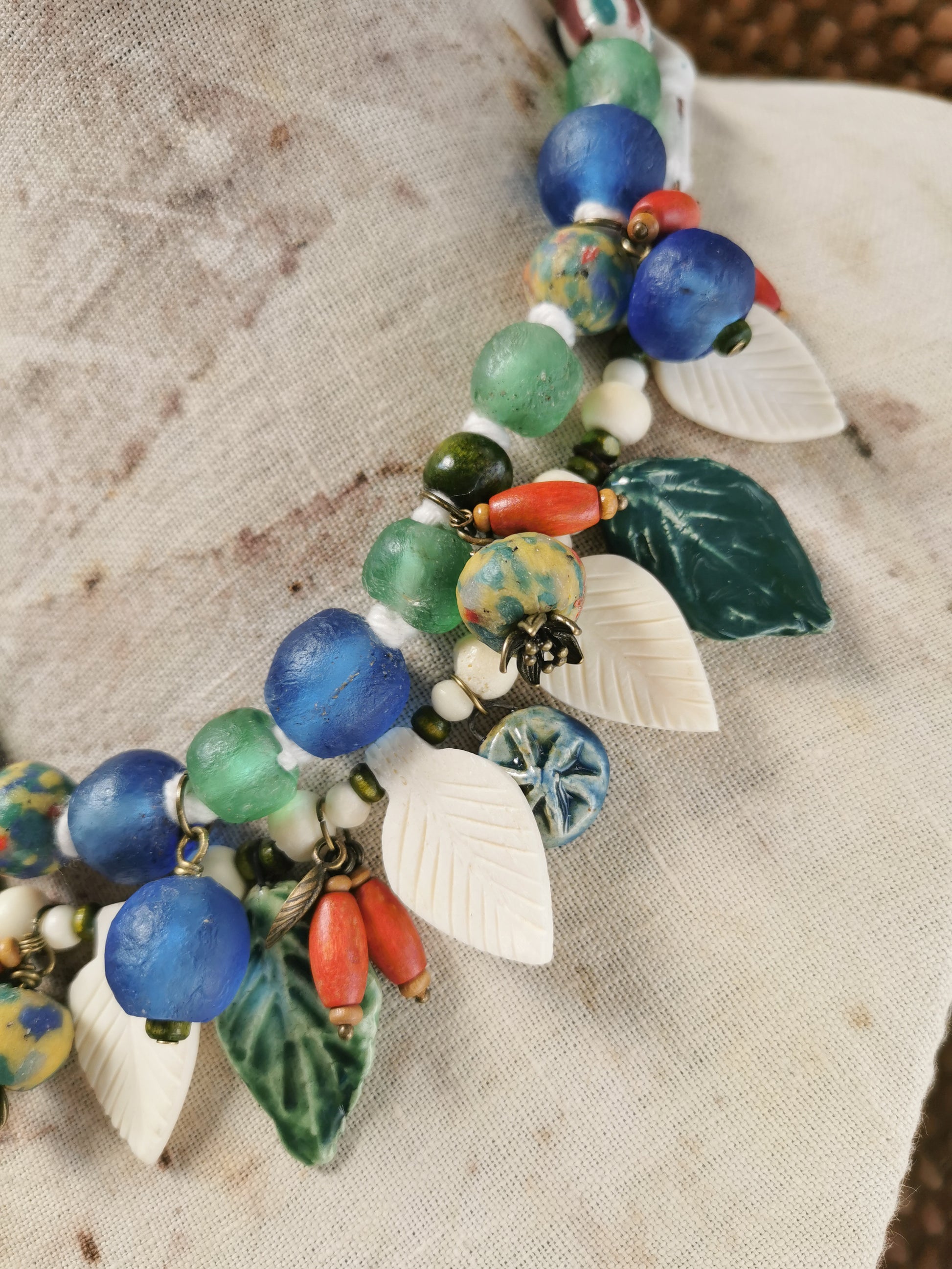 Colorful whimsical floral charm necklace  with leaf and berry charms on a textured fabric background