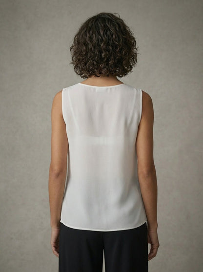 Person wearing a white sleeveless top against a neutral background