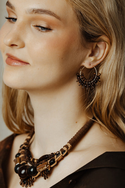 Close-up of a woman wearing a necklace and hoop earrings with a neutral background