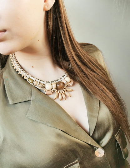 Person wearing a detailed necklace with a neutral background