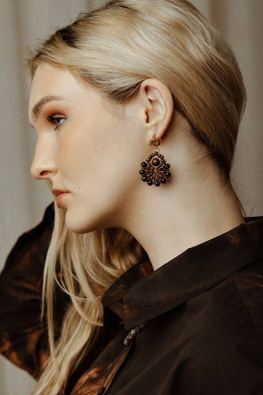 Woman wearing a dark brown coat and decorative earrings with a neutral background