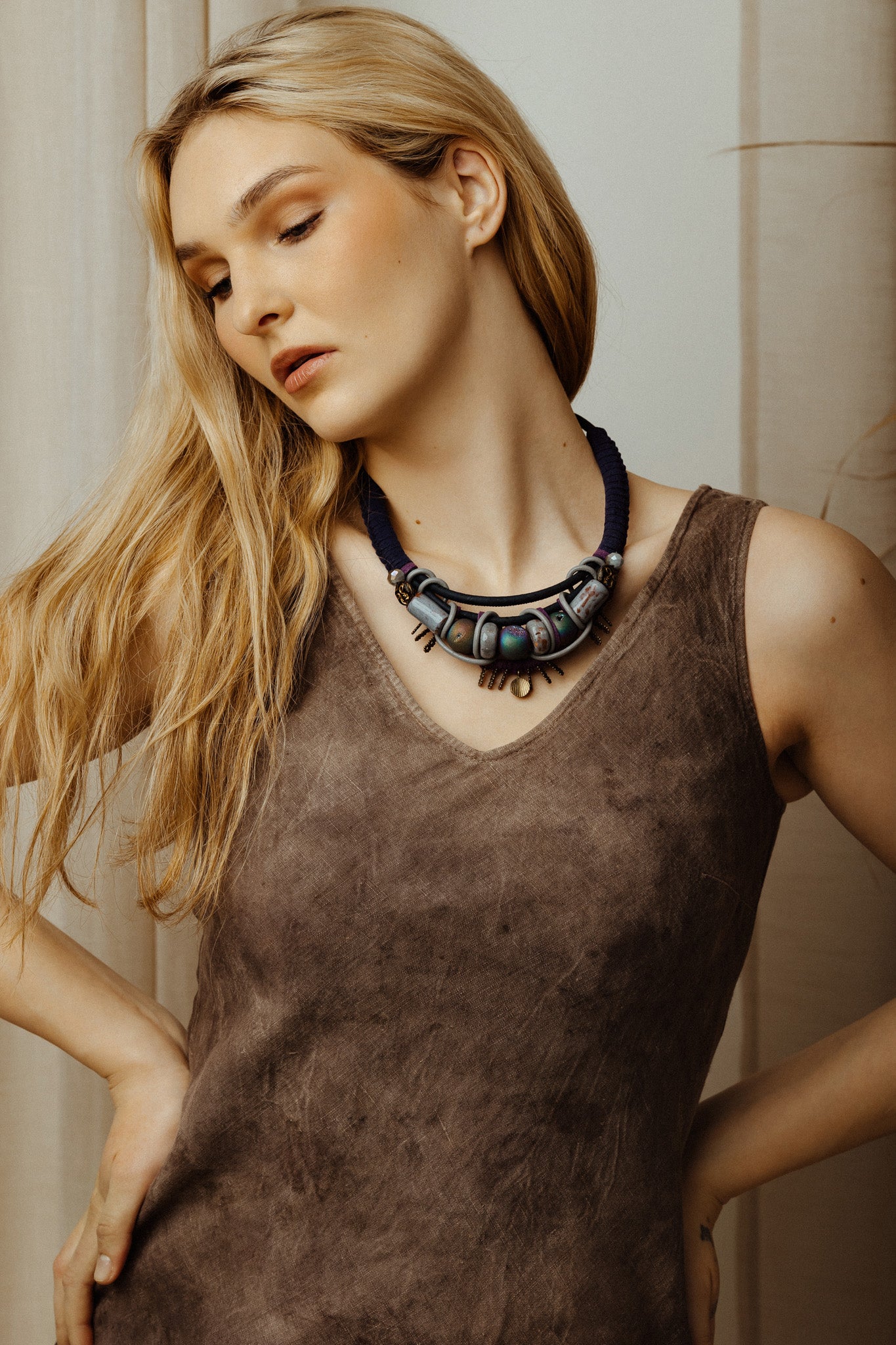 Woman wearing a brown sleeveless top and a dark necklace indoors.